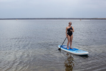 Woman stand up paddle boarding on a quiet sea with warm summer sunset colors