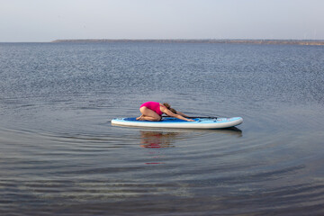 Woman doing yoga on sup board at sunset, outdoor summer activity. Sup yoga. Social Distancing. copy...