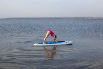 Woman practicing SUP yoga, meditating on a paddle board. Woman on sup board.