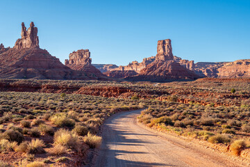 A dirt road winds through the desert with mountains in the background,Valley of the Gods Road at...