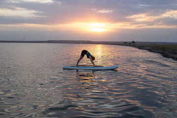 Woman practicing SUP yoga, meditating on a paddle board. Woman on sup board.