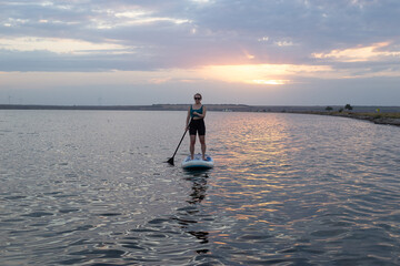 Stand up paddle boarding on a quiet sea with warm summer sunset colors