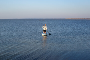 Woman on stand up paddle boarding on a quiet sea with warm summer sunrise colors