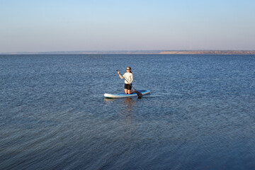 Sport woman on stand up paddle boarding on a quiet sea with warm summer sunrise colors