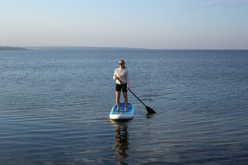 Woman standing on sup board. A beautiful young woman relaxes on a SUP board. Standup paddleboarding