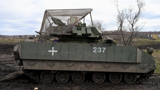 A heavily modified M2 Bradley IFV, adapted for survival on the Ukrainian front. A medical cross and anti-drone cage are key modifications for this modern battlefield.