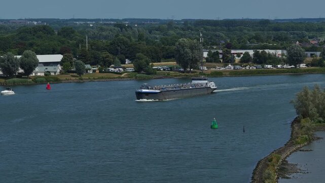 Distant aerial view of loaded Vancouver Barendrecht cargo barge sailing past countryside with buoys, Zuid-Holland, Netherlands.