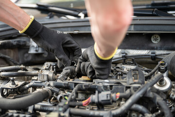 Mechanic wearing gloves fixing engine wiring inside car during repair