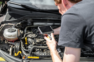 Mechanic using diagnostic tool to inspect car engine during vehicle maintenance