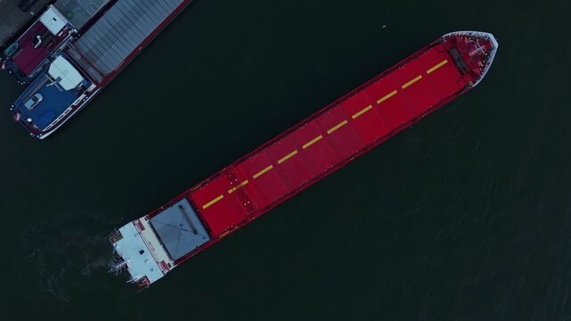 Eems River cargo ship ready to navigate on Oude Maas distributary beside industrial platform from above, Dordrecht, Zuid-Holland, Netherlands.