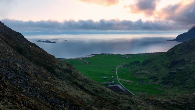 Calm aerial along Mannen cliff with view of Utakleiv beach, green fields and midnight sun