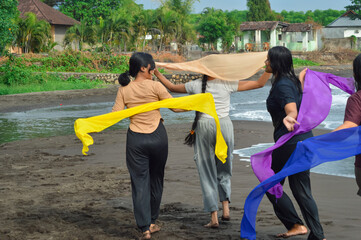 Four teenage girls walk in unison on the sandy beach near estuary water, holding scarves and...
