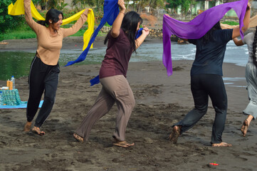 Four teenagers dash playfully across the sandy river mouth, waving colorful scarves under the...