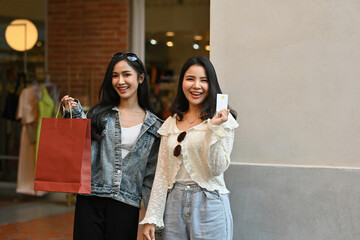 Obraz premium Two stylish Friends enjoying a shopping day, showing their shopping bag and credit card with joyful expressions