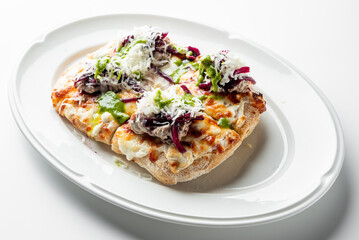 Toasted bread slices topped with melted cheese, green sauce, and shredded vegetables on a white oval plate, presented as a vibrant vegetarian appetizer.