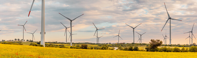 Wind turbines stand tall in a field of yellow flowers, generating clean energy against a backdrop...