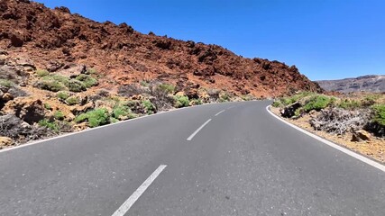 Experience a stunning view of a winding mountain road nestled in rugged terrain under a vibrant blue sky