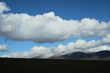 Blue sky with white clouds over mountain peaks at the end of winter