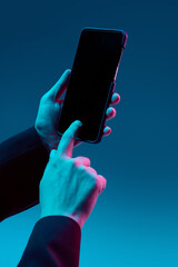 Close-up of hand tapping black copy space smartphone screen under blue and magenta light. Concept...