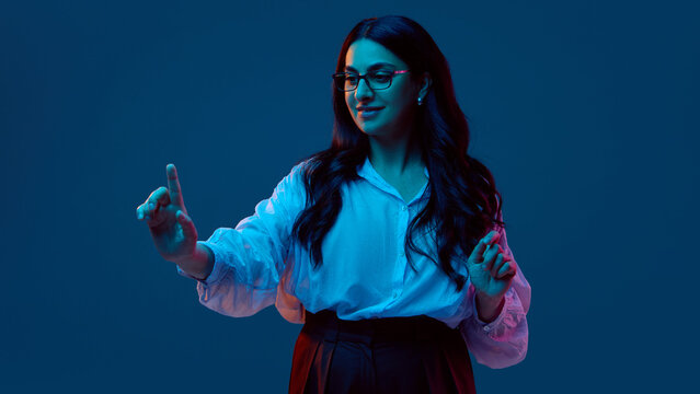 Smiling woman interacting with virtual interface under neon lighting. Concept of future UX, fintech onboarding, gesture navigation, and digital service use with optimistic engagement.