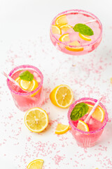 A cold pink refreshing drink with lemon and mint, chilled with ice cubes, decorated with a pink sugar rim. The best summer drink, rose lemonade on white background.