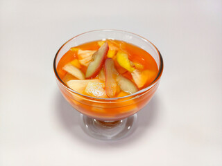Clear glass foot-stemmed bowl filled with Asinan Bogor, a vibrant orange-colored Indonesian drink...