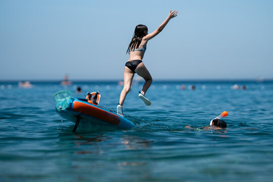 Girl jumping into the sea from paddleboard, child snorkeling