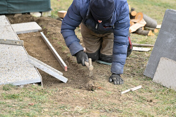 A bricklayer on his knees lays paving around a wooden house