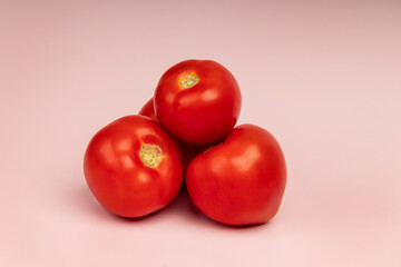 A small cluster of vibrant red tomatoes isolated on soft pink background. Minimalist composition...