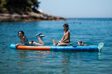 Children relaxing on paddle board in beautiful blue water