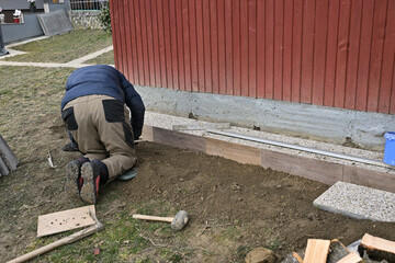 A bricklayer is laying paving stones on the sidewalk around the cottage