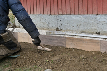 A bricklayer is laying paving stones on the sidewalk around the cottage