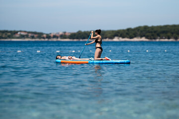 Woman paddling stand up inflatable board with girl relaxing on it