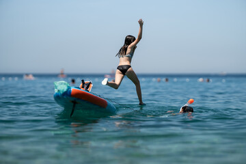 Girl jumping from paddleboard into the sea, while another girl is snorkeling