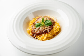 Plate of spaghetti with meat sauce and fresh basil garnish, served in a white bowl. Minimalist...