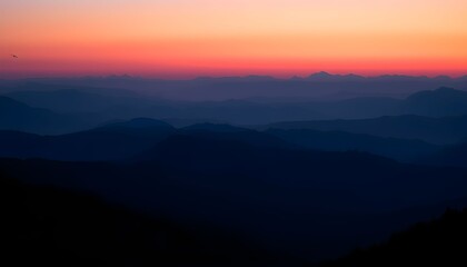 Obraz premium Layers of dark mountain silhouettes are seen against a vibrant orange and pink sunset sky.