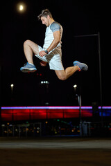 Energetic night jogger performing a jump in an urban setting with vibrant lights around