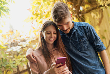 Young couple enjoys a moment together while using a smartphone in a garden during autumn