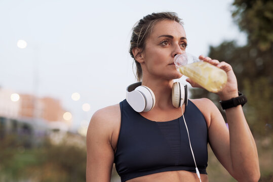 Woman in athletic attire drinking refreshing beverage during evening workout in urban setting