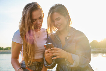 Two friends enjoying a sunny afternoon by the water while looking at a smartphone together