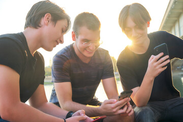 Three friends enjoying time together at sunset while interacting with their smartphones near the riverbank
