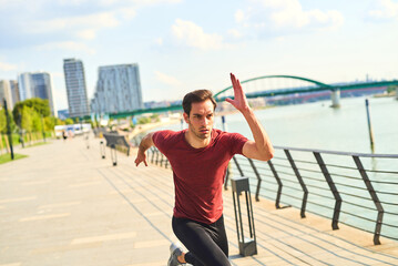Runner sprinting along the riverside promenade in a bustling city during bright daylight