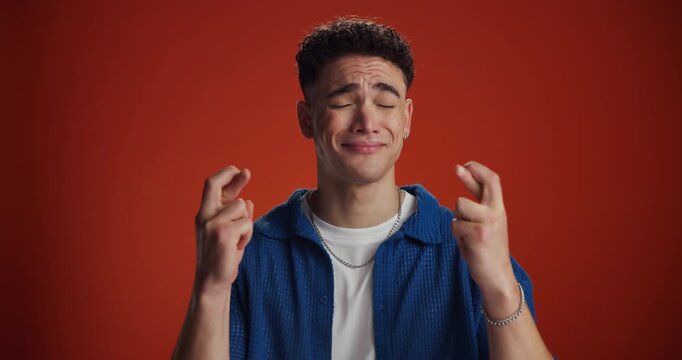 Wish, face and student with fingers crossed in studio for exam results, positive outcome or hope. Mockup, nervous man or good luck on red background for scholarship acceptance, test grade or suspense