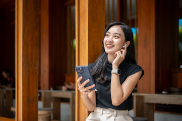 Asian woman touching earphone listening to music or on call while sit in corridor or hallway of cafe