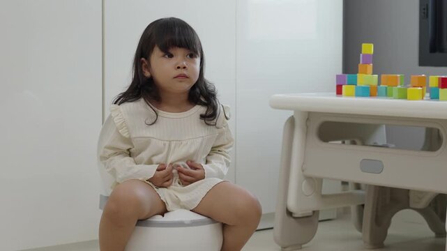 toddler gir learning sit on toilet wc seat at home. child being potty trained and suffering from stomachache and constipation