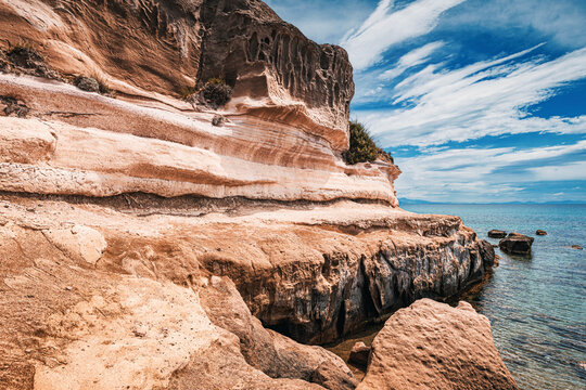 Eroded layered rocks creating a stunning cliff along the coast, basking in the warmth of a sunny summer day under a blue sky