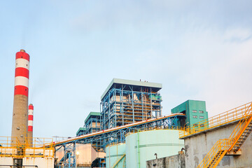 Industrial complex with chimneys and metal structures against a cloudy sky landscape showcasing...
