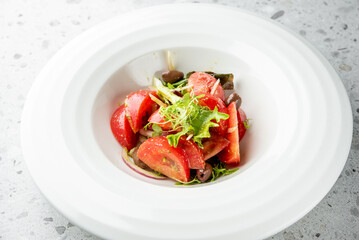 Fresh vegetable salad with tomatoes, olives, onions, and leafy greens in a white bowl on a light surface. Healthy, vibrant, and perfect for vegetarian or vegan diets.