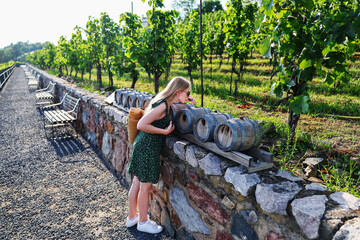 Stylish young woman in green dress leaning over rustic wine casks in vineyard setting.
