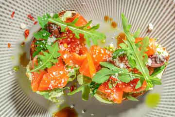 Toasted bread topped with fresh arugula, avocado spread, smoked salmon, olives, and grated cheese for a vibrant and savory appetizer. top view